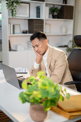 Asian businessman looking worried as resting head on hand in front of laptop at office working table