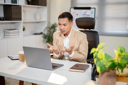 Asian businessman looking shocked or disappointed as opening both palm at laptop on office's table.