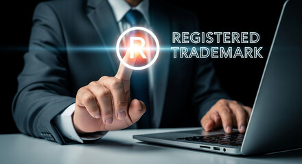 Man in suit touching registered trademark icon on laptop screen with a finger on white surface