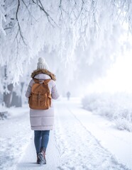 A woman in a cozy winter coat strolls down a snow-covered road, her breath visible in the crisp air, surrounded by frosted trees and a serene landscape.