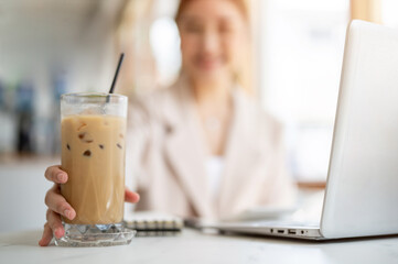 Close up of woman hand holding or grabbing iced coffee on glass coaster aside laptop on cafe's table