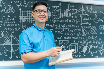 Asian male teacher holding book and chalk in front of math blackboard, education, classroom and teaching concept