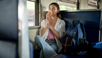 Pretty asian woman holding coffee drinking or sipping as sitting on carriage bench at train station. © bongkarn