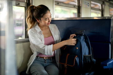 Pretty asian woman opening or zipping up blue bag while sitting on carriage bench at train station.