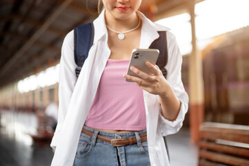 Close up woman with bag holding and looking at smartphone while standing or walking at train station