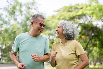 Glasses old man and old woman smiling or laughing while running or jogging together inside the park.