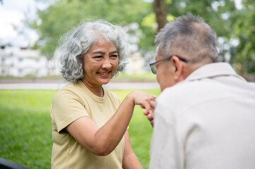 Obraz premium Close up of old woman smiling at old man holding or kissing her hand while sitting together in park.