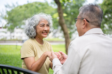 Obraz premium Close up of an old woman smiling at old man while holding hand and sitting together on bench in park