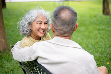 Close up of old woman smiling and looking at glasses old man while sitting together on bench in park