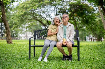 Old woman smiling as hugging glasses wearings man's shoulder while sitting together on bench in park