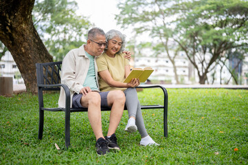 Glasses old man holding hugging woman shoulder reading book together while sitting on bench in park
