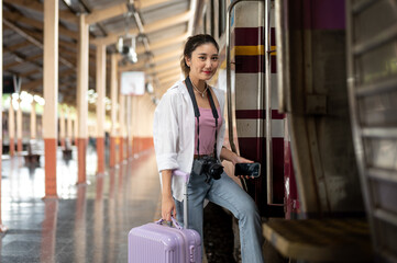 Asian woman with camera holding phone and luggage as walking into carriage at train station platform