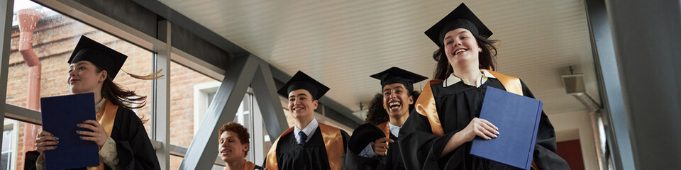 Header of group of multiethnic young people wearing graduation caps and gowns walking together...