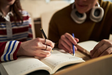 Caucasian young woman and Caucasian young man studying together at university, writing notes in...