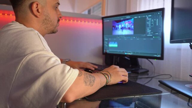 Side view of man adjusting color nodes and wheels on editing software interface while working at home desk with daylight and LED lighting