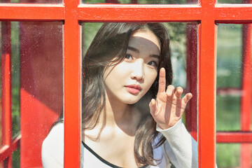 Young Asian Female Looking Through Red Phone Booth Glass Window