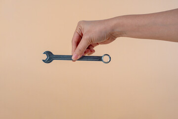 Hand holding a wrench isolated on cream background.