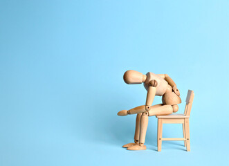 Wooden Model Sitting Bent Over with One Hand on Back – Visual Metaphor for Pain or Physical Fatigue