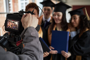 Group of multiethnic young men and women wearing graduation caps and gowns standing together posing...