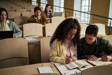 Group of multiethnic university students sitting in lecture hall, young adults collaborating on...