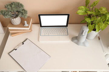 Blank laptop with books and plants on table in office