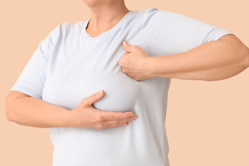 Mature woman checking her breast on beige background, closeup. Cancer awareness concept