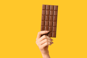 Female hand with chocolate bar on yellow background