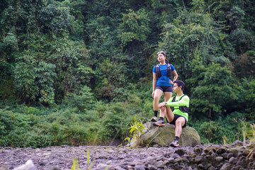 Asian Couple Resting on Trail Run in Rocky Forest Landscape