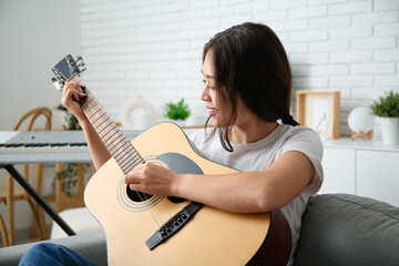 Fototapeta premium Pretty young woman playing guitar at home