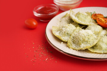 Plate of tasty ravioli with tomatoes and cheese on red background