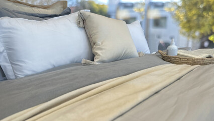 cozy bed with soft pastel-colored bedding and pillows. with   tray with a lotion bottle  and book