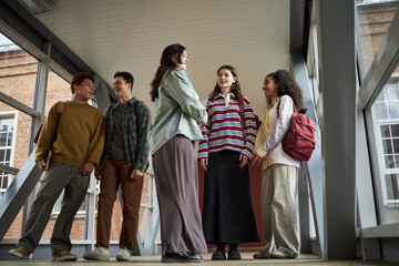 Group of multiethnic university students standing in hallway talking and smiling, young adult men...