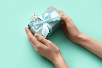 Female hands with gift box and gypsophila flowers on turquoise background. International Women's Day