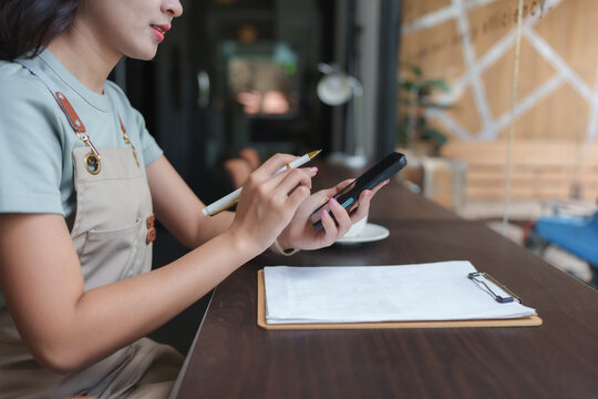 Coffee shop owner managing inventory and orders using smartphone and clipboard