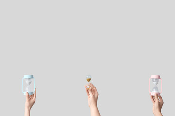 Female hands holding hourglasses on grey background