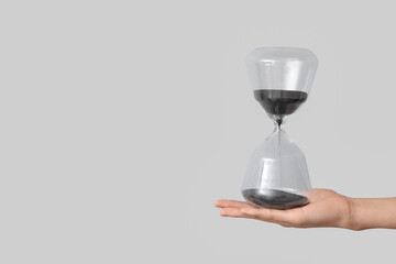 Female hand holding hourglass on grey background