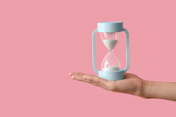 Female hand holding hourglass on pink background