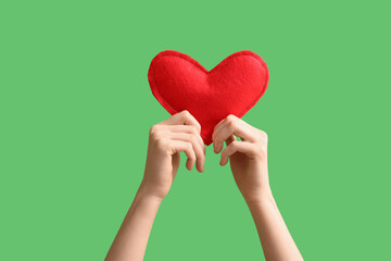 Obraz premium Female hands with red heart on green background, closeup. Valentine's Day celebration