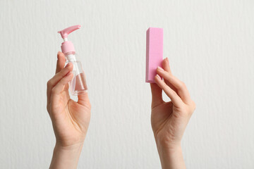 Female hands with bottle of cuticle oil and buffer on white background