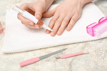 Female hands holding cuticle oil pen with towel and manicure instruments on grey grunge background