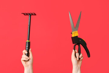 Female hands with gardening rake and secateurs on red background, closeup