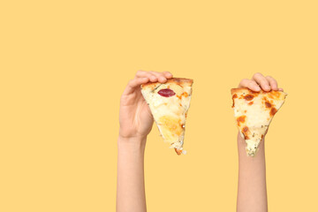 Female hands holding tasty pizza slice on yellow background