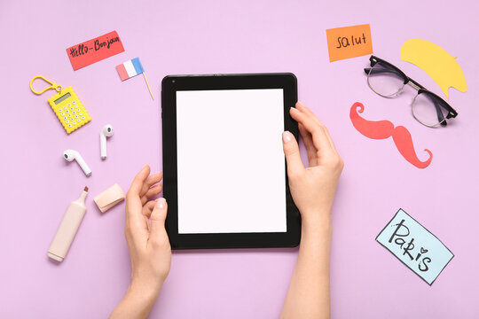 Female hands with modern tablet computer, stationery and French words on color background - Powered by Adobe