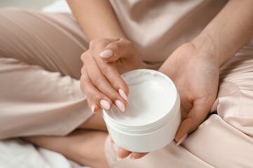 Woman in silk pajamas holding jar of cream, closeup