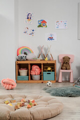 Stylish interior of modern playroom  with large pouf, toys and pictures on wall