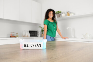 Beautiful young African-American woman with basket of ice cream on table in kitchen