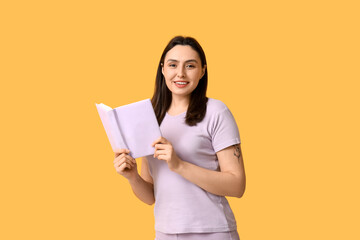 Young happy woman with book on orange background