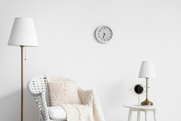 Stylish living room with armchair, lamp and clock on white wall