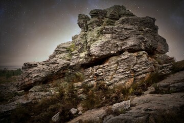 Flat design layered rock formation is rising on hillside under starry sky with shrubs and lichens
