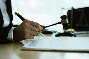 Lawyer sitting at desk in modern office reviewing and signing legal documents related to finance,...